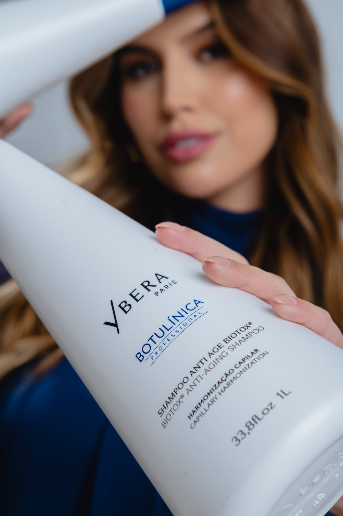 Mujer de cabello castaño sosteniendo un envase blanco de champú Botulínica de Ybera Paris de 1 litro.-83